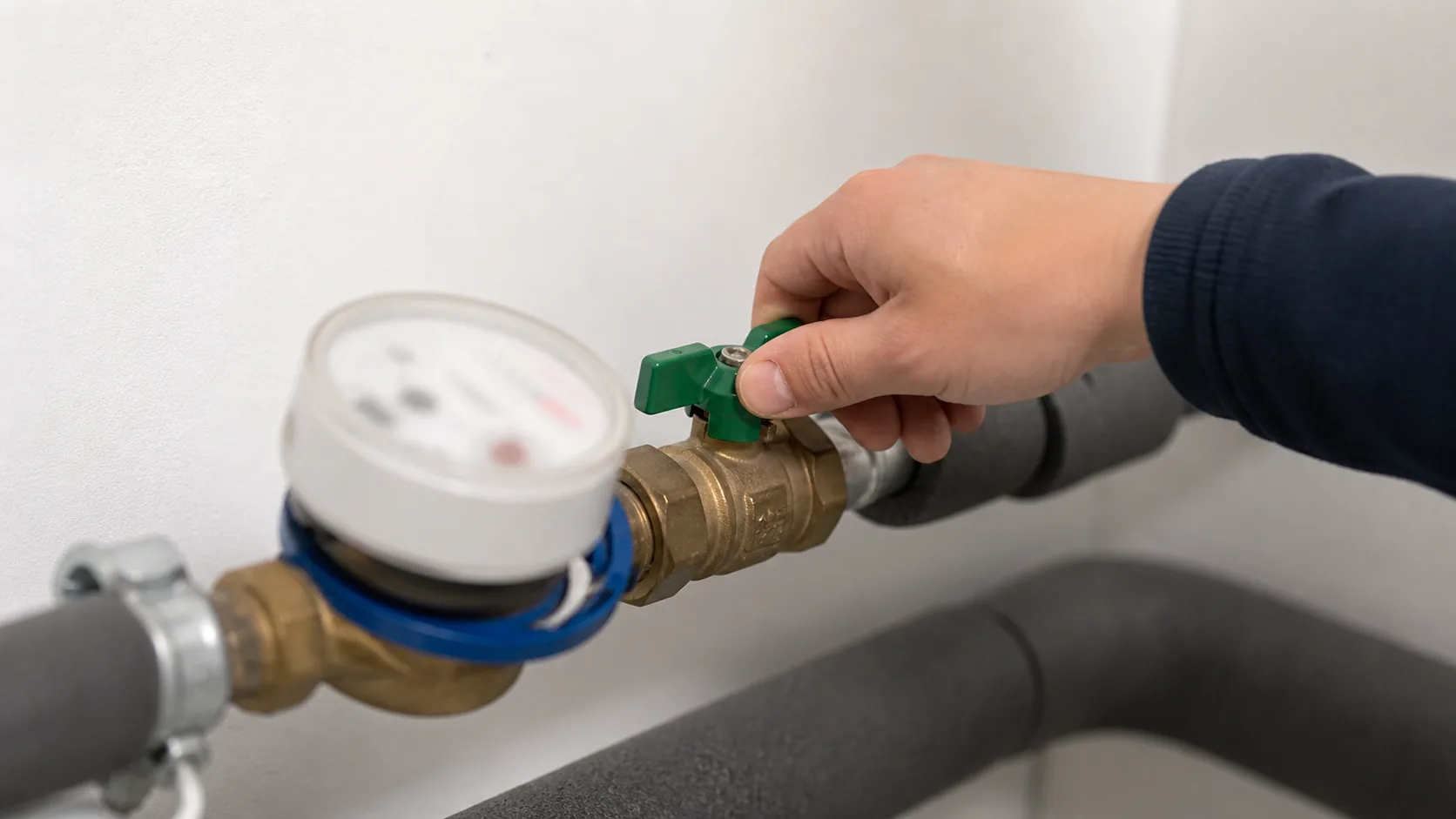 Hand schließt ein Absperrventil nach dem Wasserzähler, Wasserzähler ohne lesbare Nummern im Hintergrund